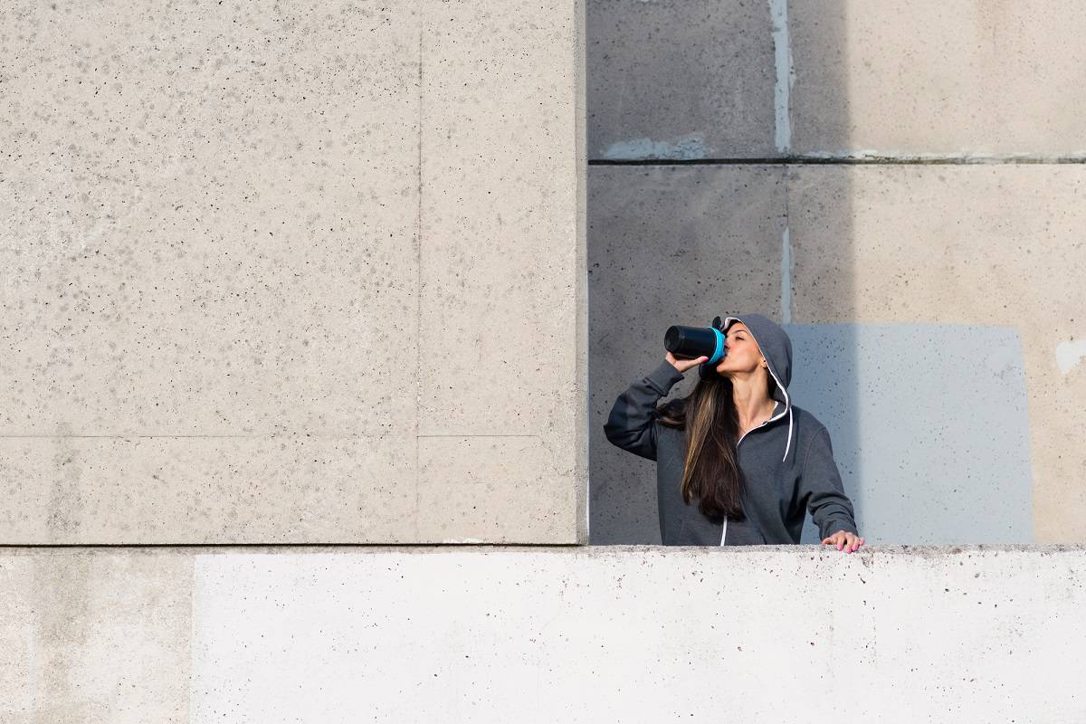 A woman standing outside drinking a protein shake after her workout.