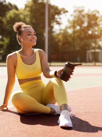 A female runner sitting on a track with a protein shake in her hand.