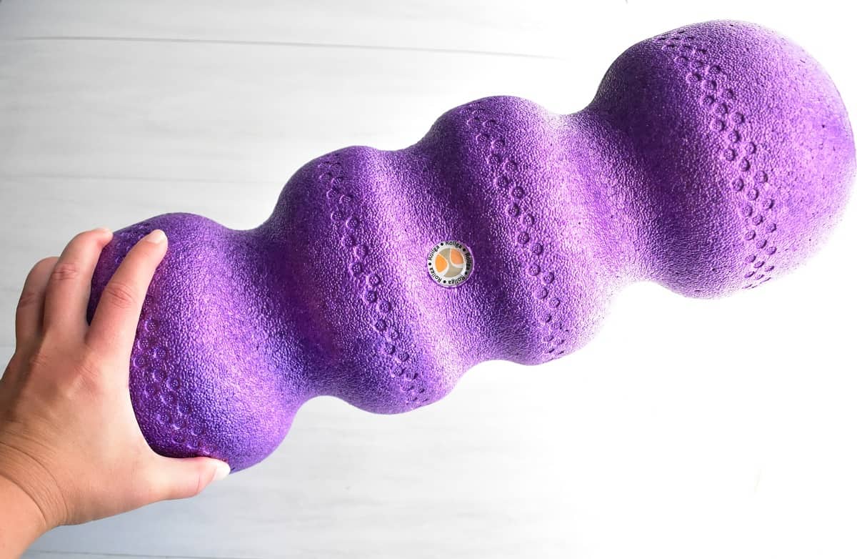 A woman's hand holding a purple Rollga foam roller.