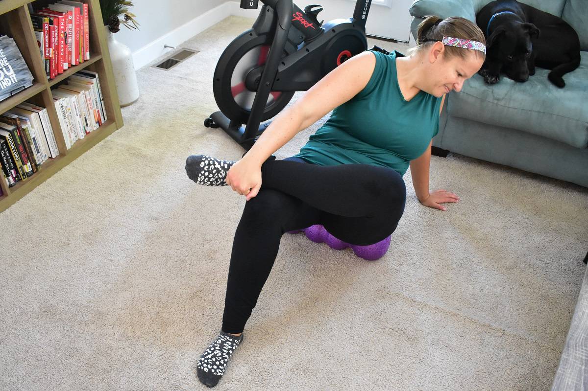 A woman rolling her glute muscles on a foam roller.