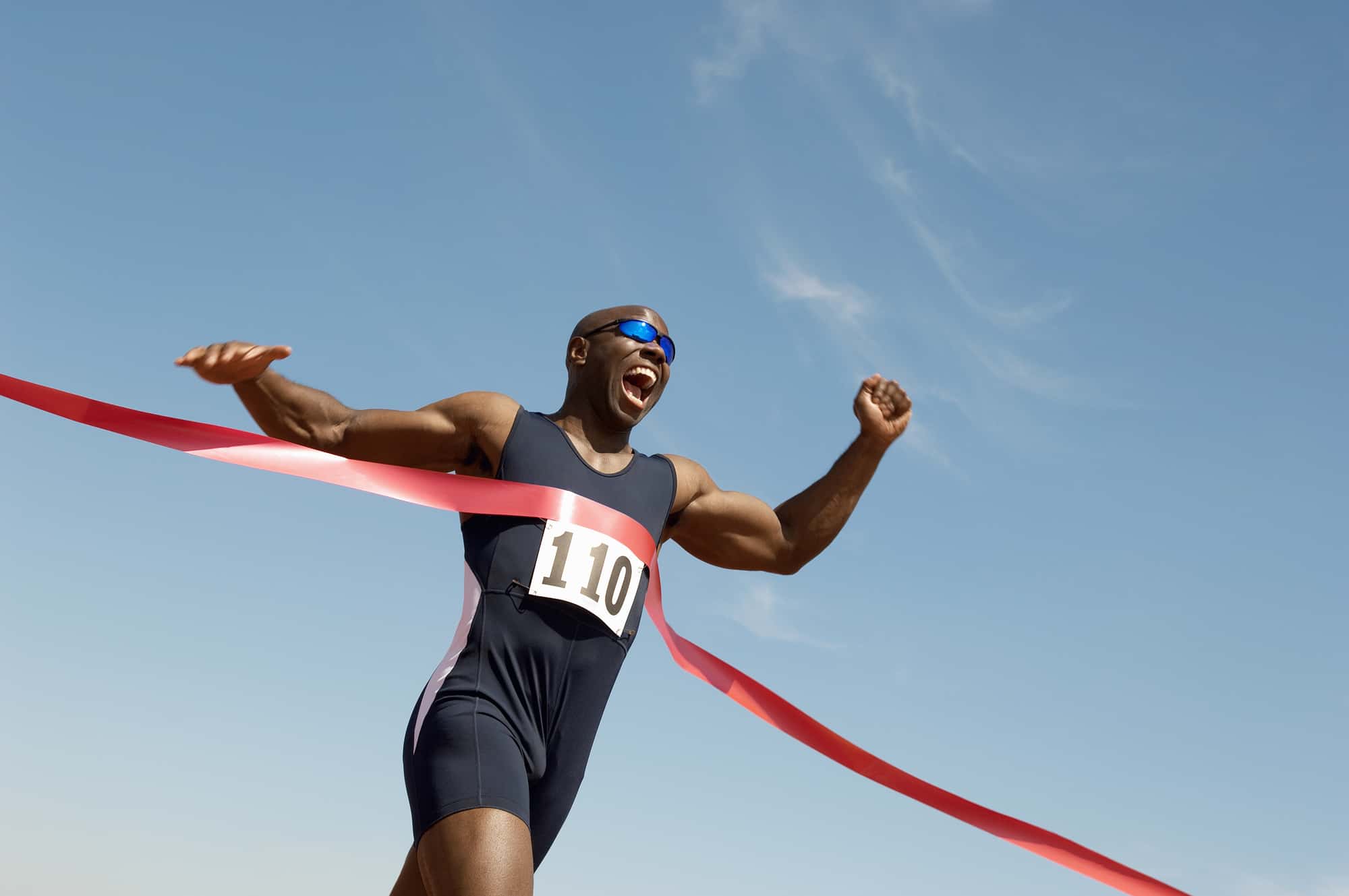 A man crossing a red finish line tape for a running PR.