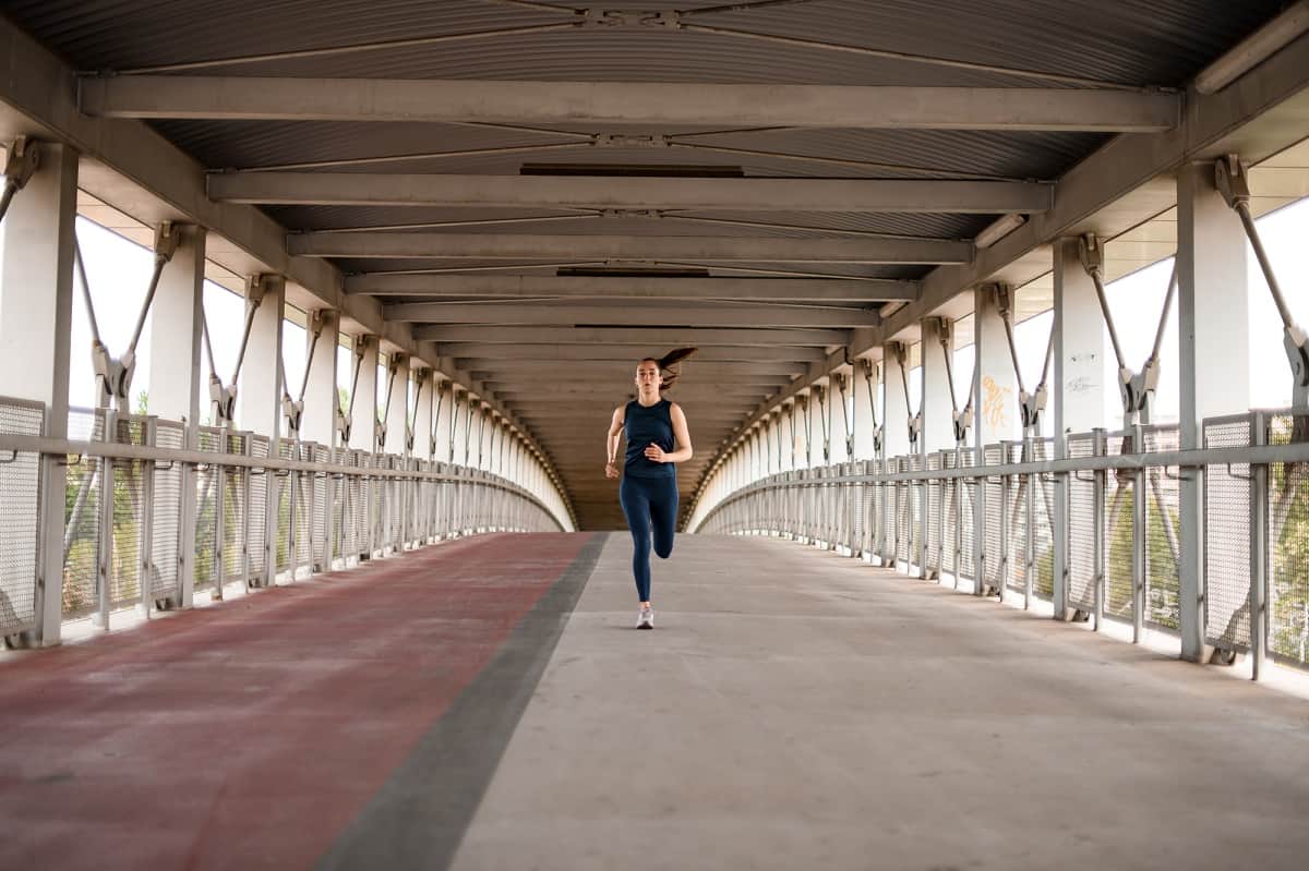 A woman running underneath a bridge on a paved path.