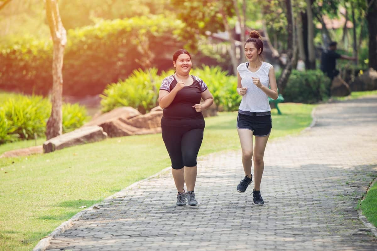 Two women running outside along a path next to greenery.