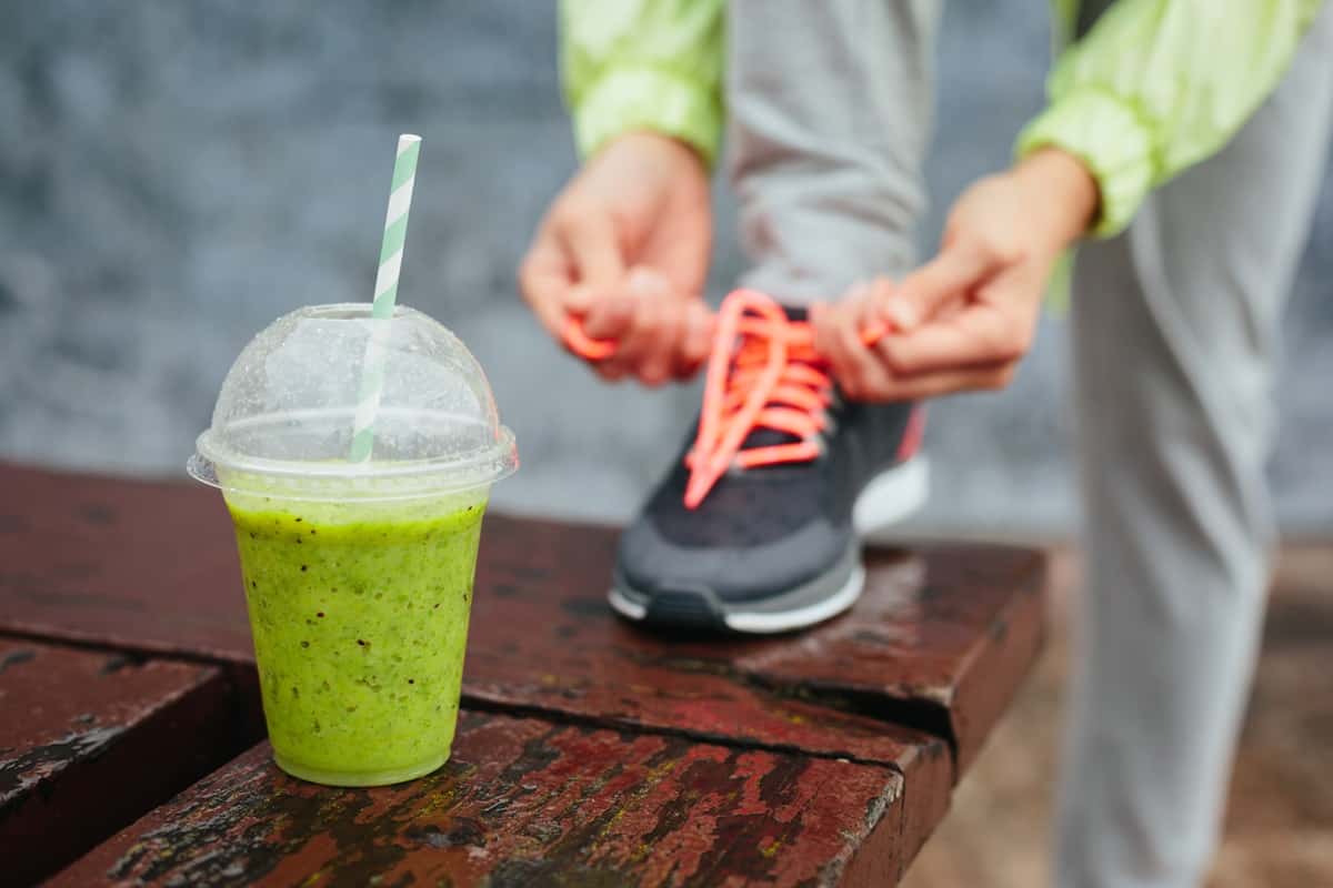 A smoothie next to a woman tying her shoe.