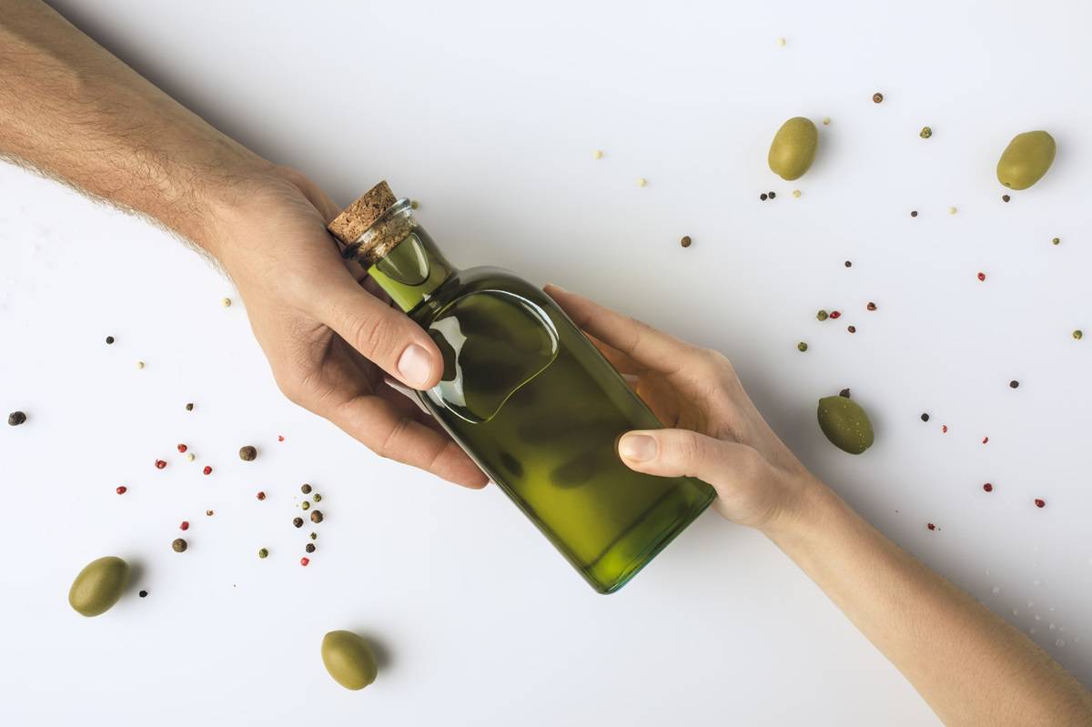 Two hands holding a bottle of olive oil.