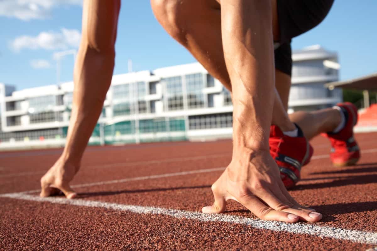 A close up of a runner's hands and feet at the start of a sprint on a track.
