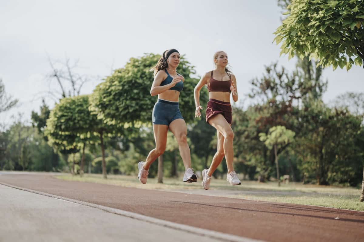 Two female runners outside on a track.