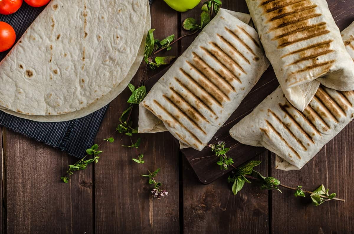 Several breakfast burritos on a wooden board.