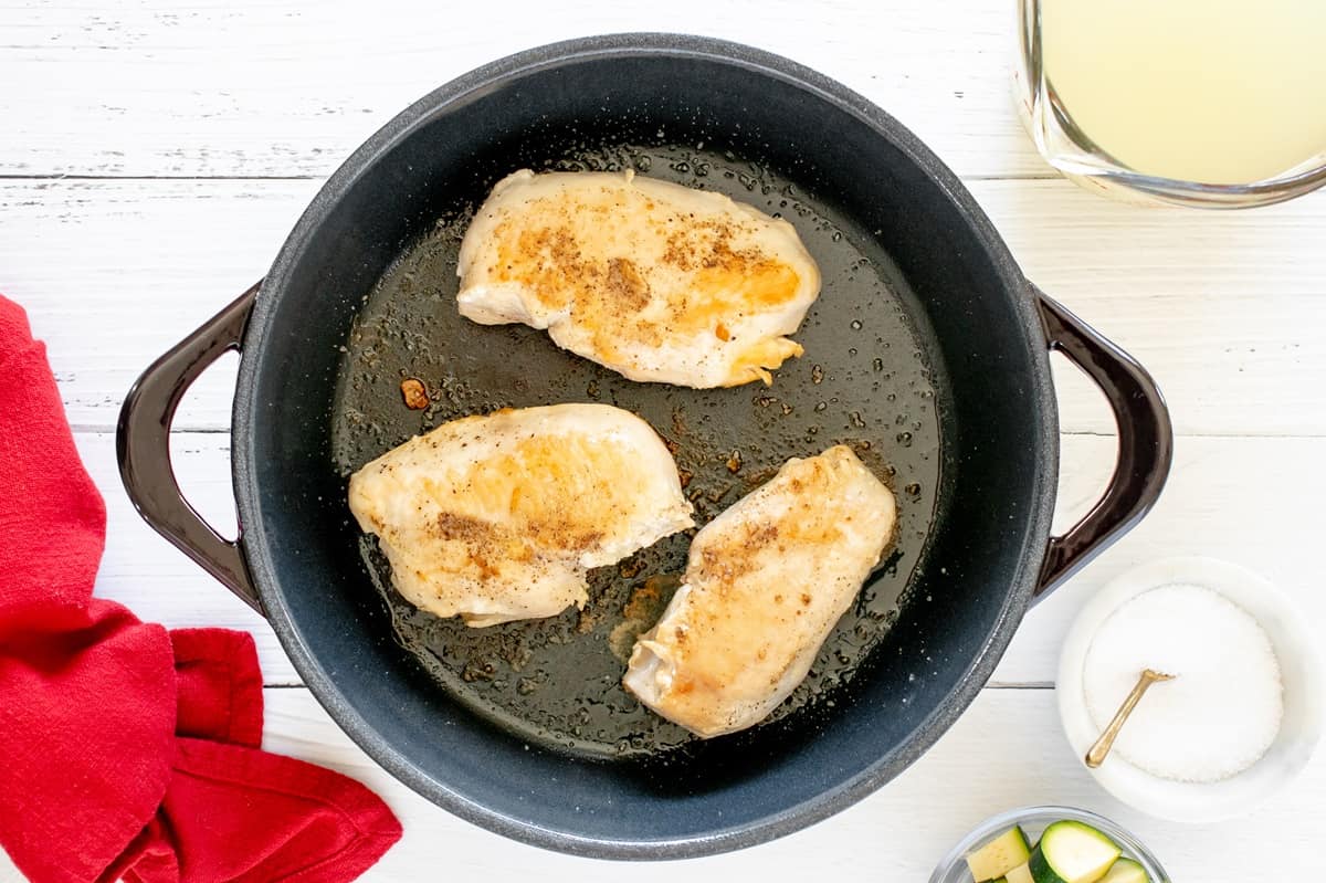 A few chicken breasts being seared in a pot.