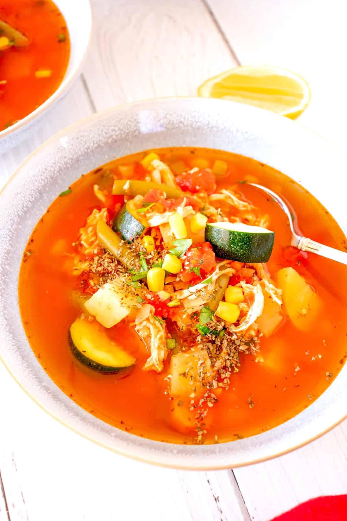 A bowl of tomato vegetable chicken soup with a spoon in the bowl.