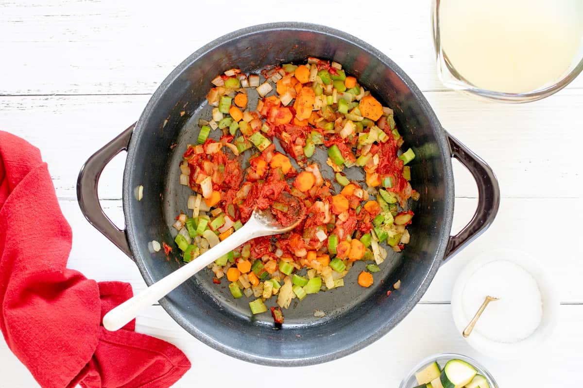 Tomato paste and seasoning added to vegetables in a pot.