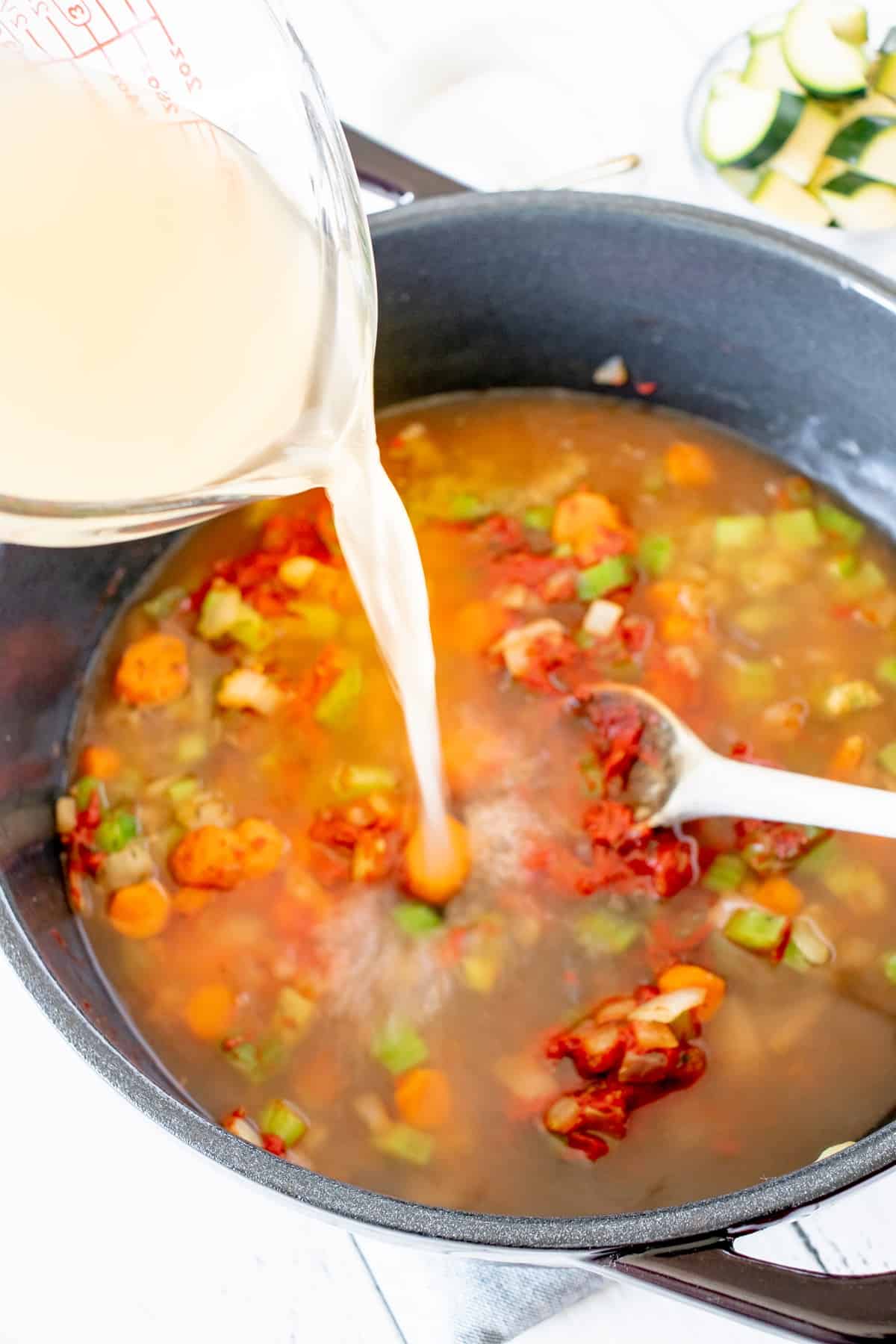 Broth being poured from a measuring cup into a pot.