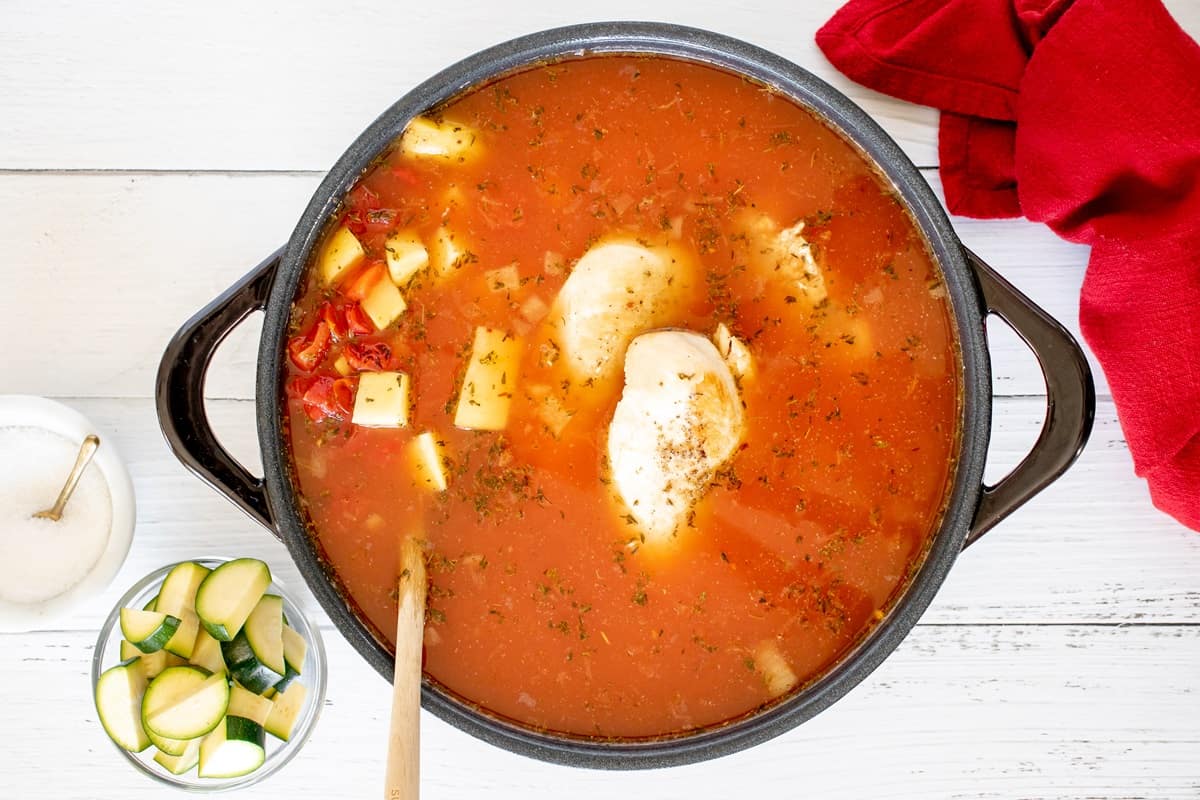 Chicken breast cooking in the soup mixture in a pot.