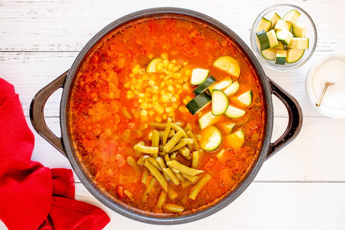 Zucchini, corn, and green beans added to a pot of soup.