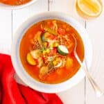 A bowl of chicken vegetable soup with a spoon in it and a red napkin next to the bowl.