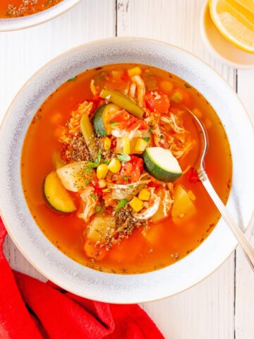 A bowl of chicken vegetable soup with a spoon in it and a red napkin next to the bowl.