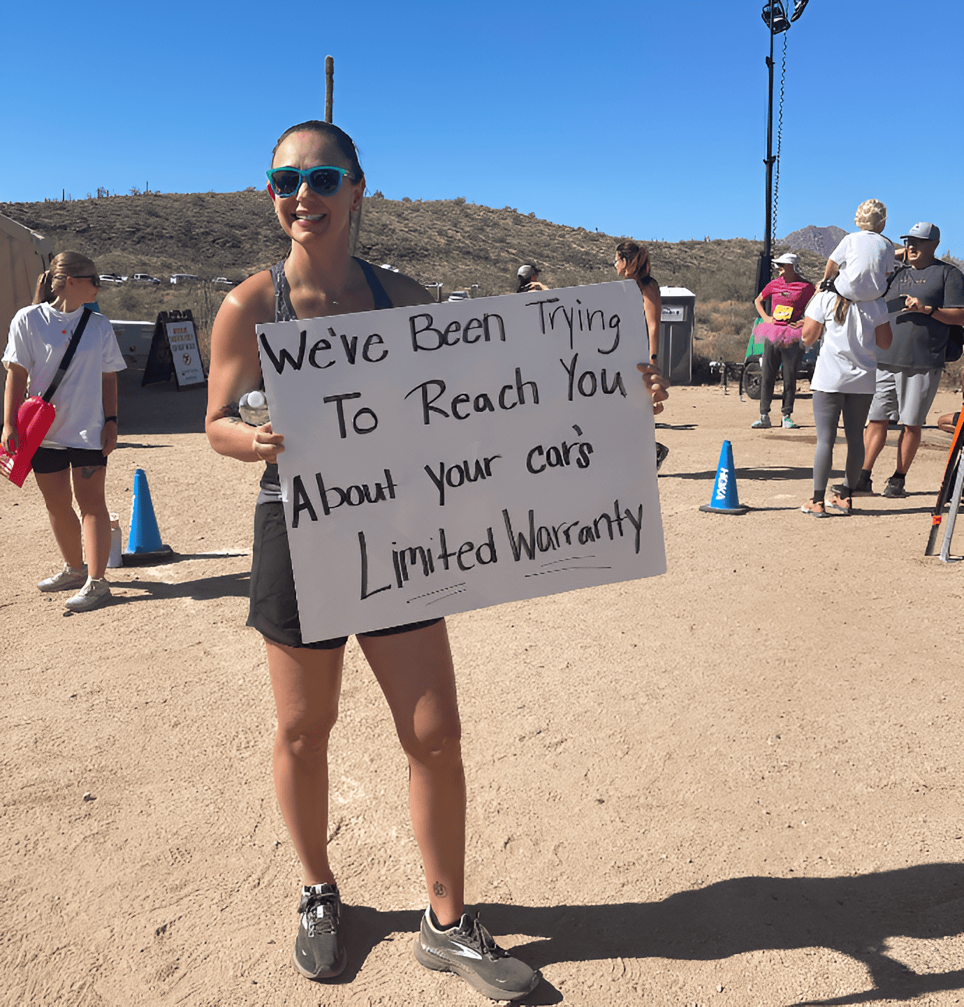 A woman holding a race day sign that says we've been trying to reach you about your car's limited warranty. 