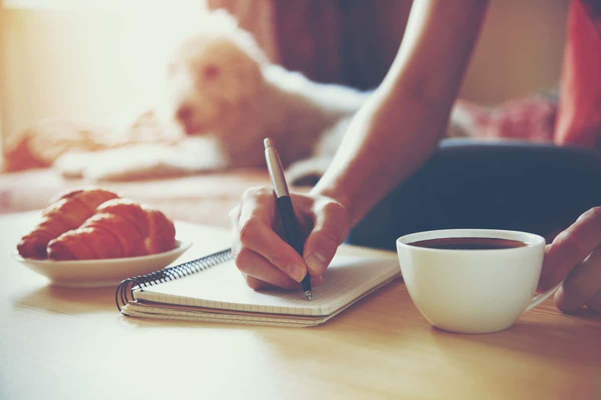 A woman journaling and drinking coffee as part of her morning routine.