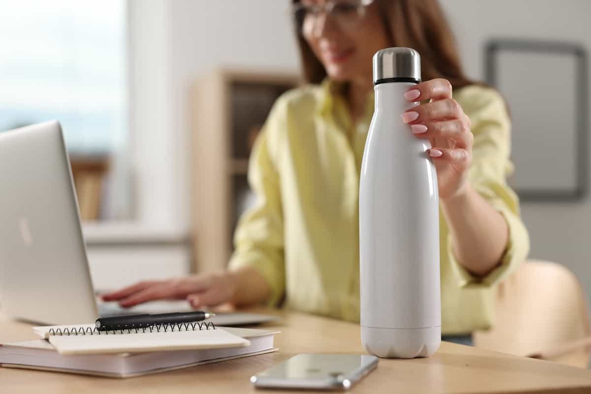 A woman holding her water bottle at her desk as part of her new years resolution to drink more water.