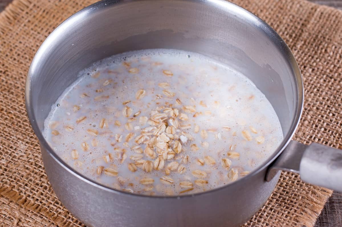 Cooking oatmeal with milk in a silver pot.