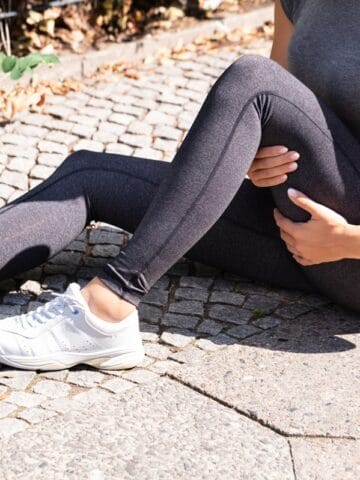 A runner sitting on the ground pointing out their hamstring.