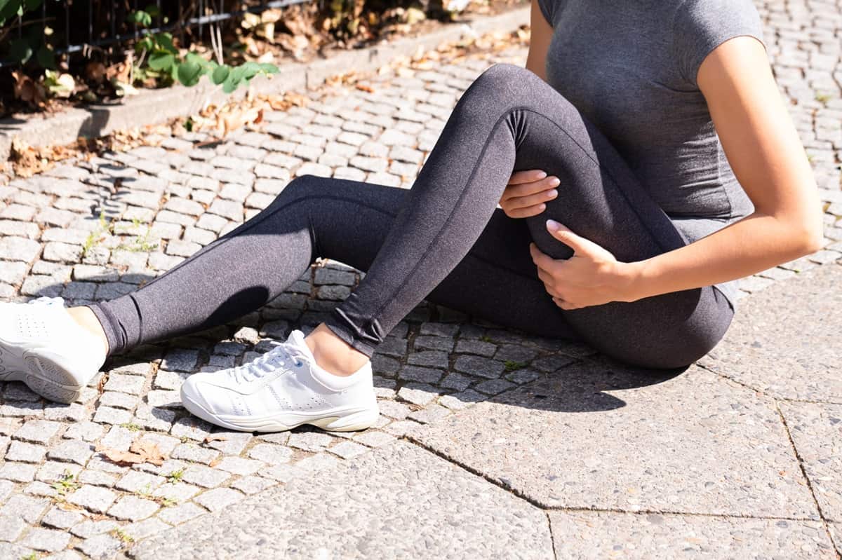 A runner sitting on the ground pointing out their hamstring.