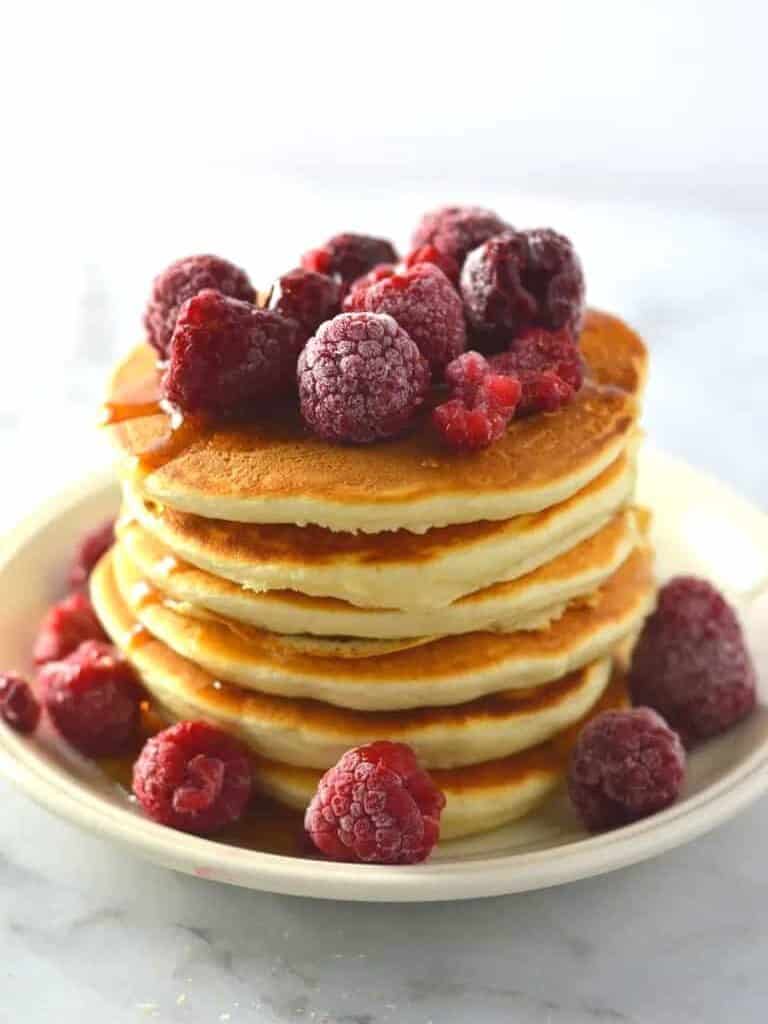 A stack of vanilla protein powder pancakes topped with raspberries.