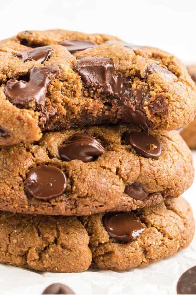 A stack of three protein chocolate chip cookies, with one having a bite taken out of it.
