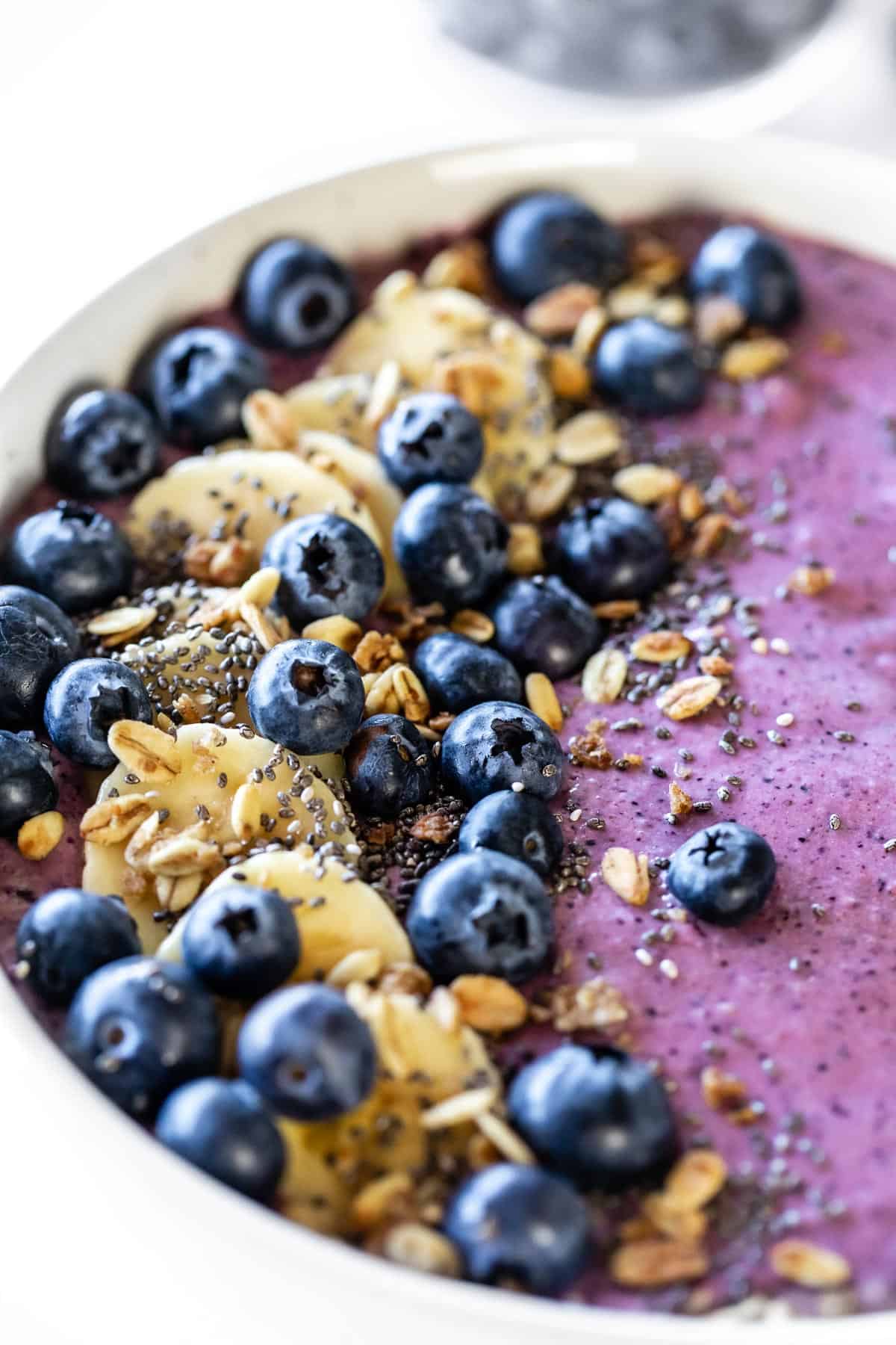 A close up of banana, blueberry, and granola toppings on a blueberry smoothie bowl.