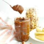 A spoon scooping out homemade healthy chocolate hazelnut butter from a jar.
