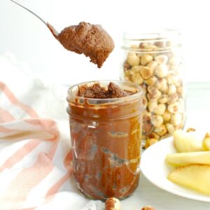 A spoon scooping out homemade healthy chocolate hazelnut butter from a jar.