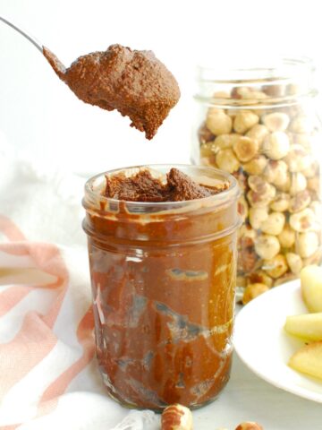 A spoon scooping out homemade healthy chocolate hazelnut butter from a jar.