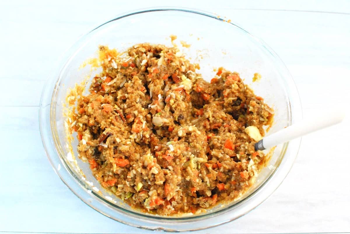 Muffin batter in a glass bowl after the apple, carrots, zucchini, coconut, raisins, and nuts have been folded in.