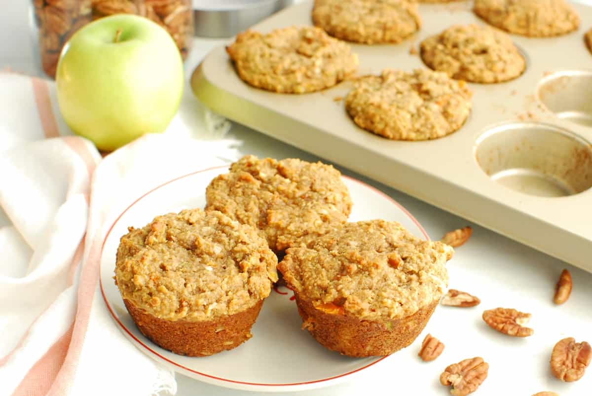 Some almond flour morning glory muffins on a plate next to a napkin, apple, and muffin tin.