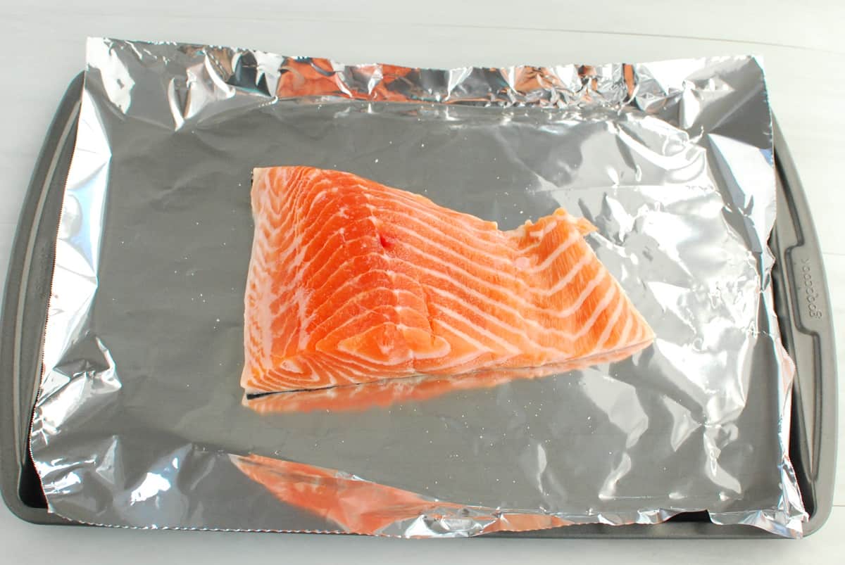 A salmon fillet on a foil-lined baking sheet.