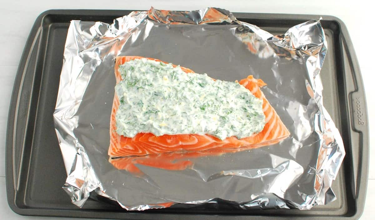 Herbed yogurt sauce spread on top of a salmon fillet.