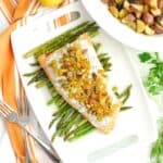 Herbed yogurt topped salmon on top of roasted asparagus on a white platter.