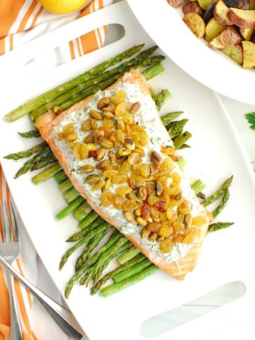 Herbed yogurt topped salmon on top of roasted asparagus on a white platter.