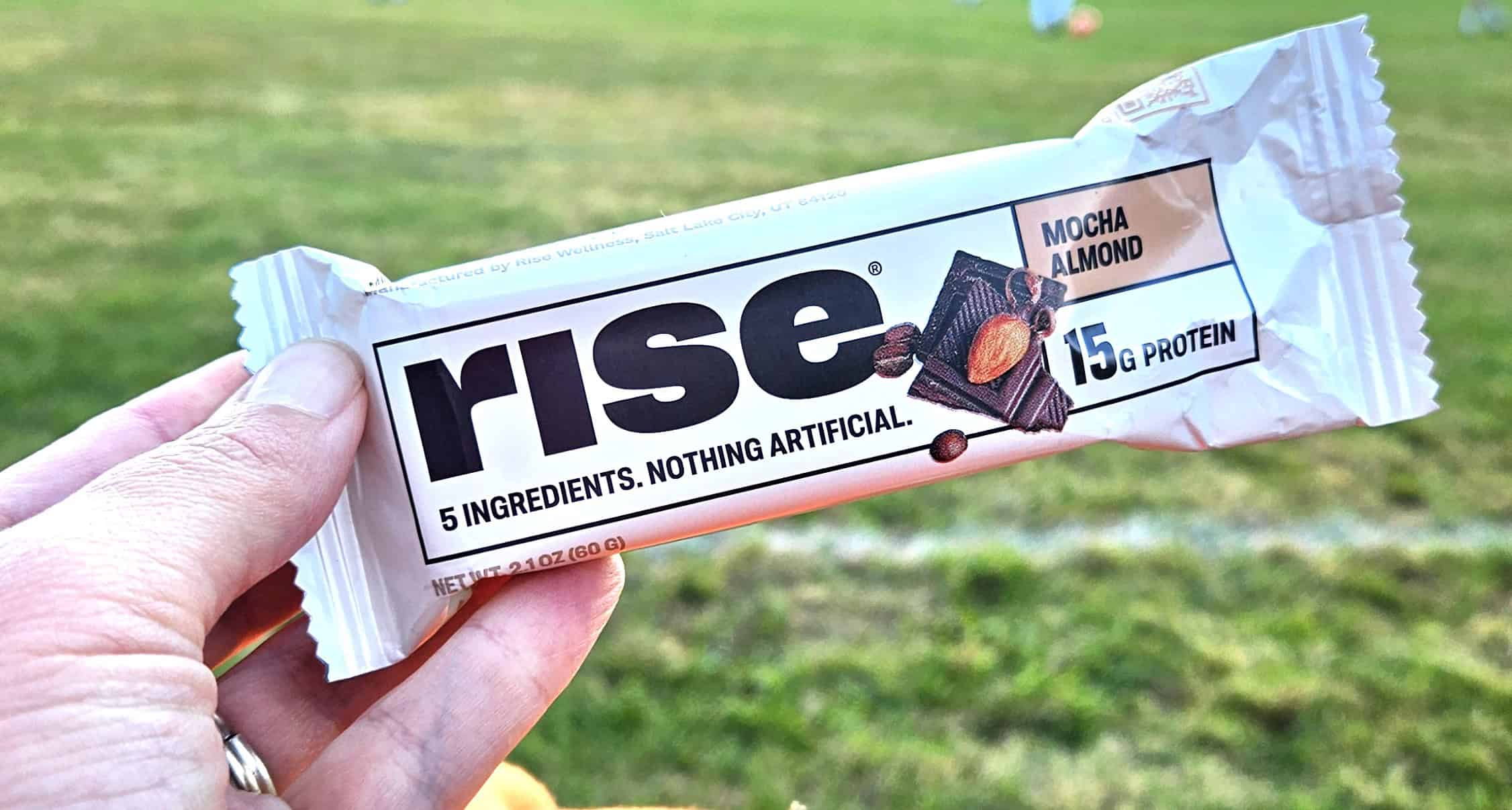 A woman's hand holding a Rise protein bar.