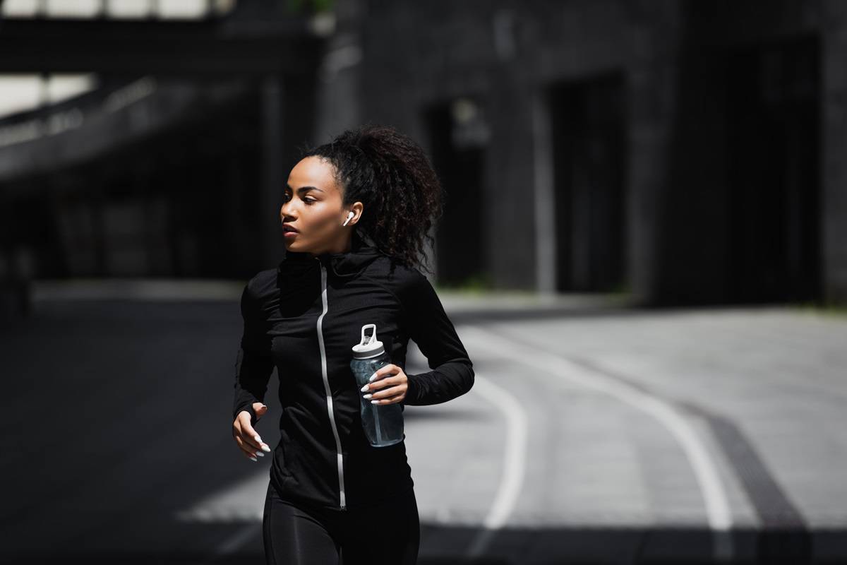 A female runner outside on a path holding a water bottle.