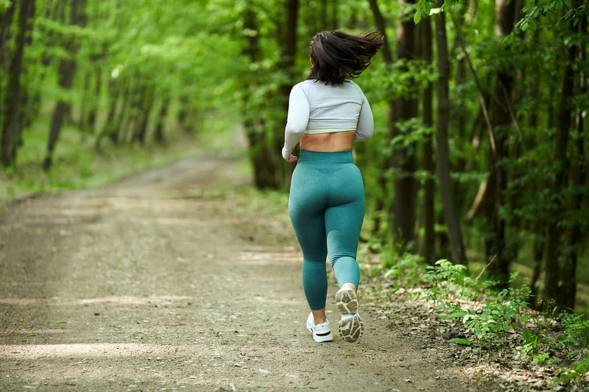 A woman running in sneakers along a dirt road.