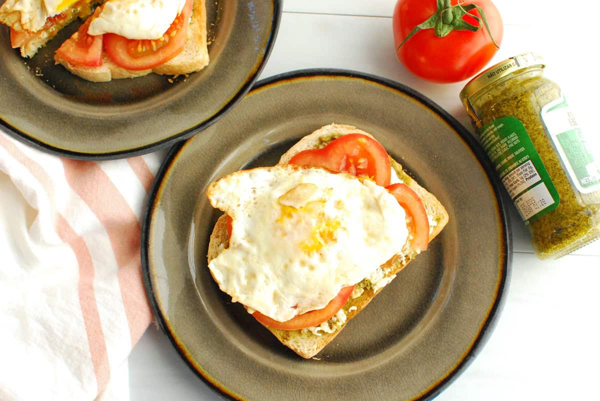 Pesto burrata toast with sliced tomato and a fried egg on a plate.