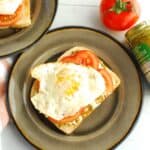 Pesto burrata toast topped with tomato and egg on a plate.