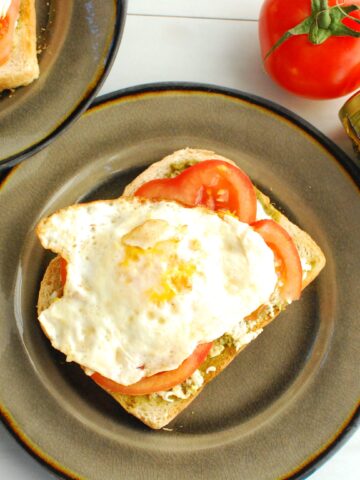 Pesto burrata toast topped with tomato and egg on a plate.