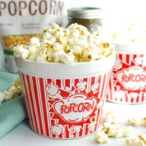 An overflowing bowl of dill pickle popcorn, with some kernels falling onto the table.
