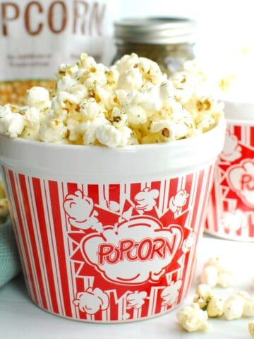 An overflowing bowl of dill pickle popcorn, with some kernels falling onto the table.