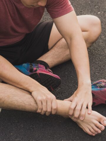 A man grasping his bare foot with an injury outside after running.