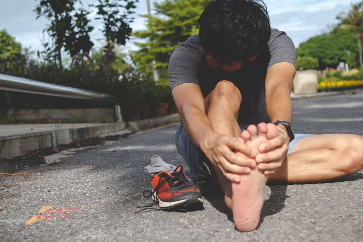 A man stretching his foot while sitting outside.