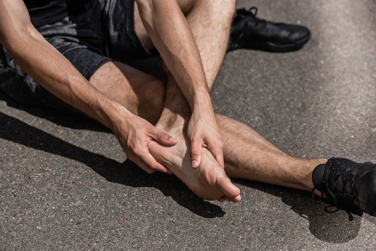 A man feeling his foot outside as he's dealing with a running foot injury.