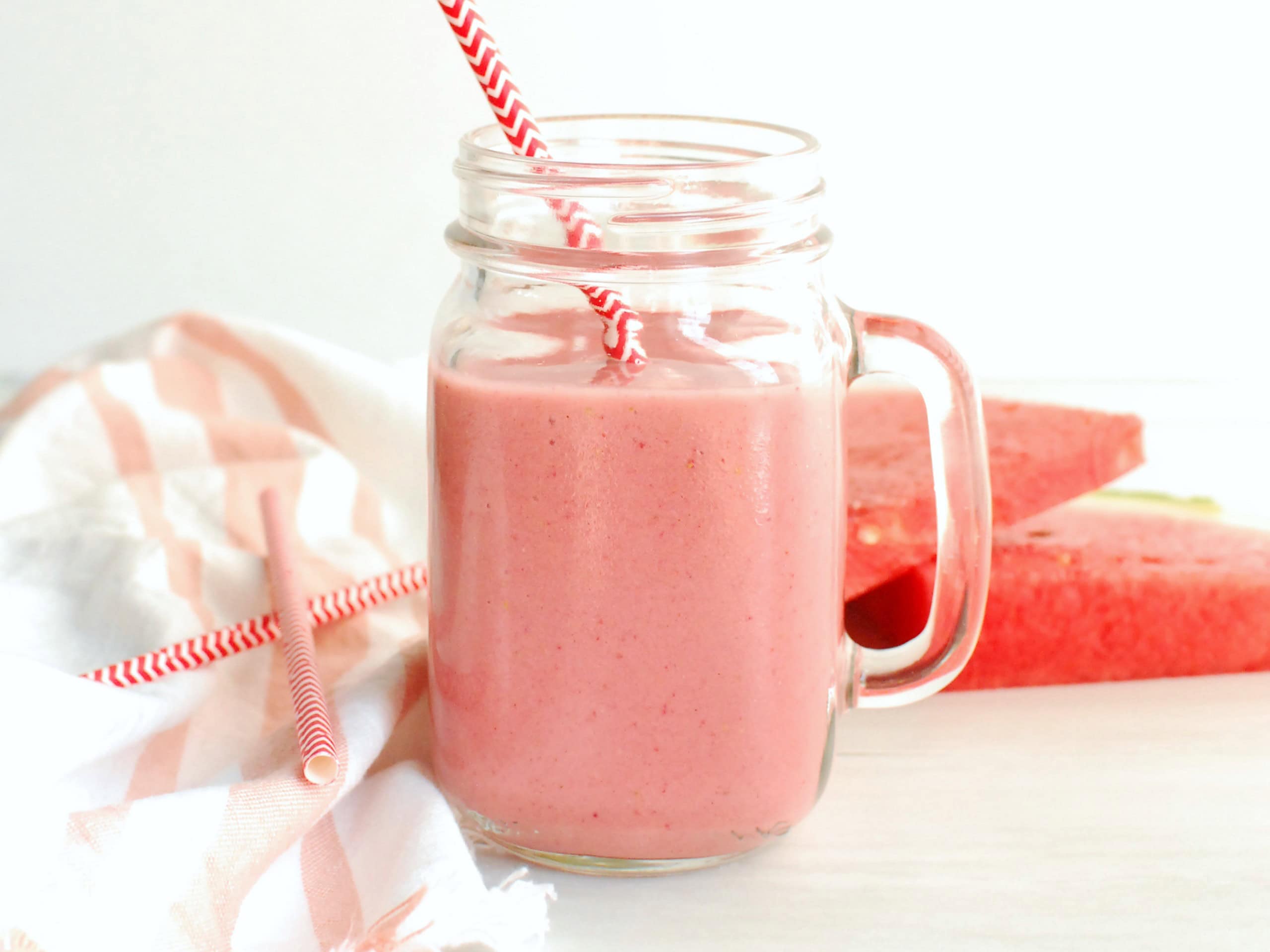 A mason jar glass filled with a strawberry watermelon smoothie.